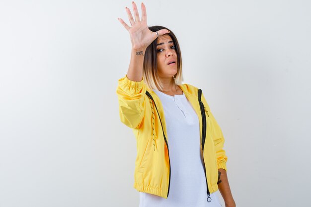 白いTシャツ、黄色のジャケットで一時停止の標識を示し、自信を持って、正面図を表示している若い女の子。