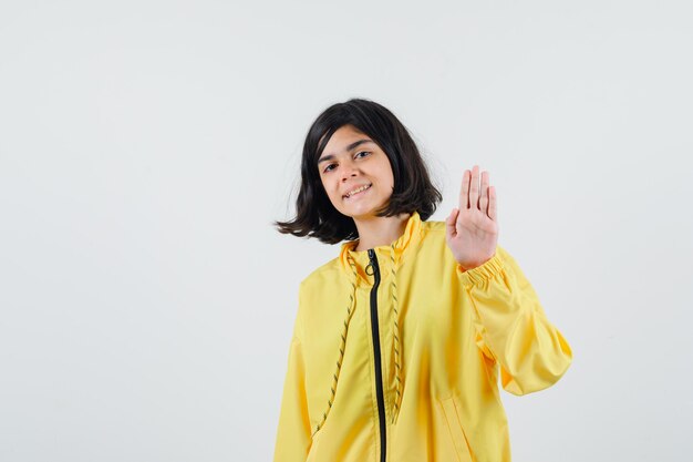 Young girl showing stop sign in yellow bomber jacket and looking happy.
