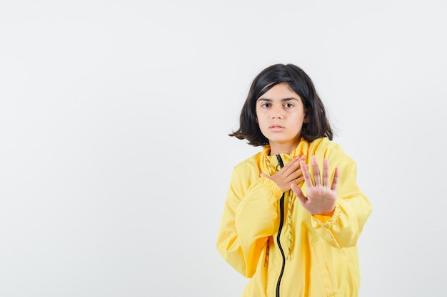 Young girl showing stop sign in yellow bomber jacket and looking serious