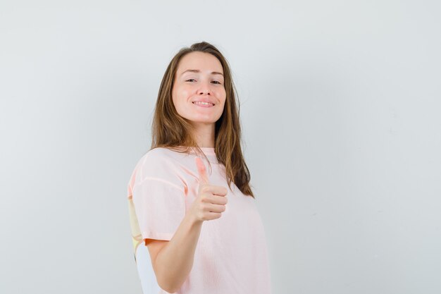 Молодая девушка показывает палец вверх в розовой футболке и выглядит уверенно