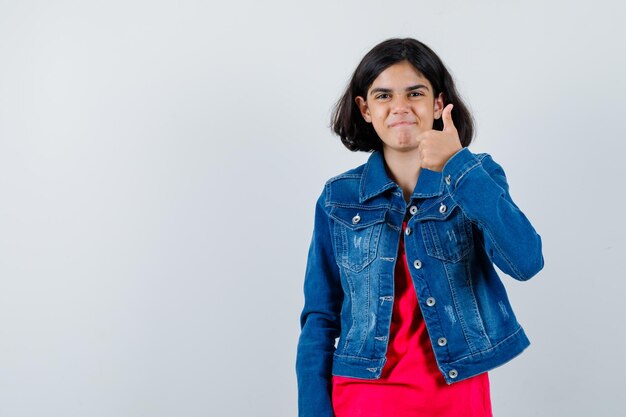 Young girl showing thumb up in red t-shirt and jean jacket and looking happy , front view.