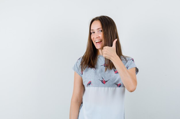 Young girl showing thumb up in t-shirt and looking glad. front view.