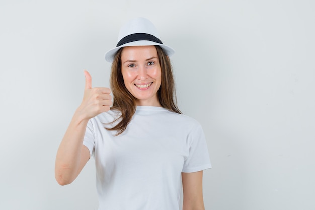 Молодая девушка показывает палец вверх в белой шляпе футболки и выглядит радостной