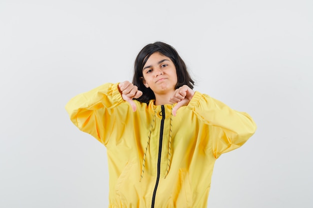 Young girl showing thumbs down with both hands in yellow bomber jacket and looking displeased