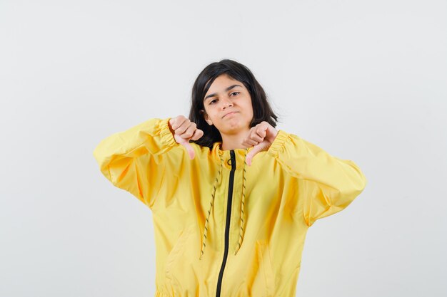 Young girl showing thumbs down with both hands in yellow bomber jacket and looking displeased