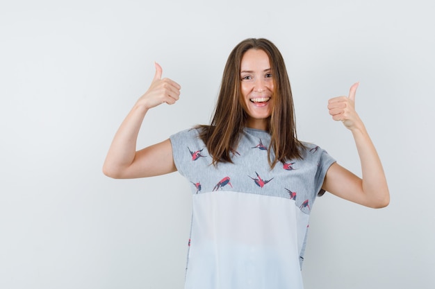 Young girl showing thumbs up in t-shirt and looking happy , front view.