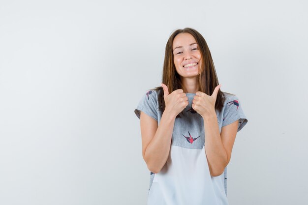 Young girl showing thumbs up in t-shirt and looking happy , front view.