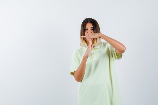 Young girl showing time-break gesture in t-shirt and looking serious. front view.