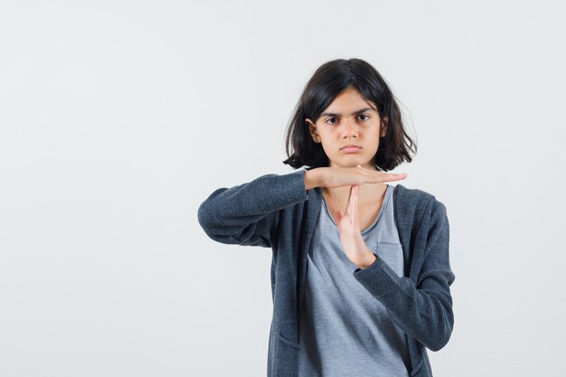 Young girl showing time break in light gray t-shirt and dark grey zip-front hoodie and looking cute.