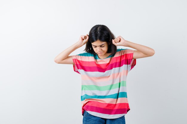 Молодая девушка показывает жест победителя в красочной полосатой футболке и выглядит серьезным, вид спереди.