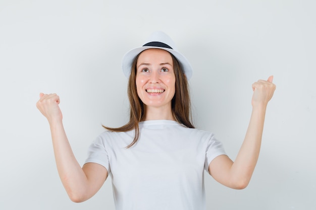 Young girl showing winner gesture in white t-shirt hat and looking blissful  