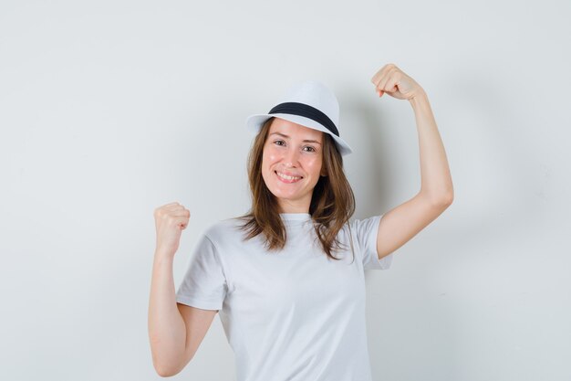Молодая девушка показывает жест победителя в белой футболке и выглядит удачливой