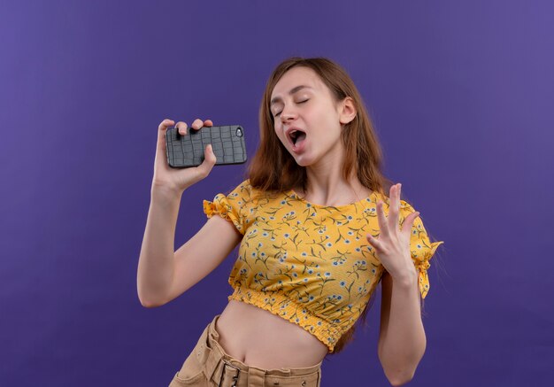 Young girl singing using mobile phone as microphone on isolated purple wall
