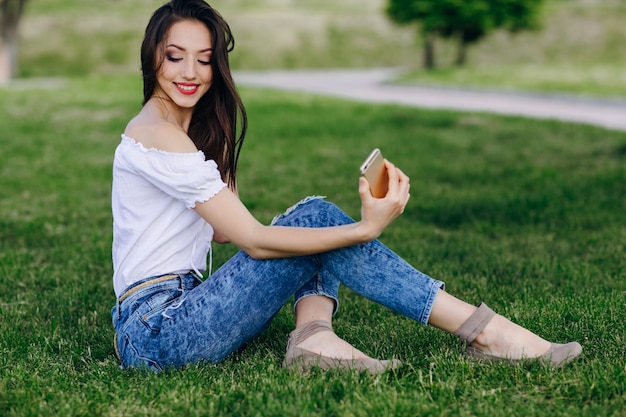 Young girl sitting in a park making an auto photo while smiling and touching her hair