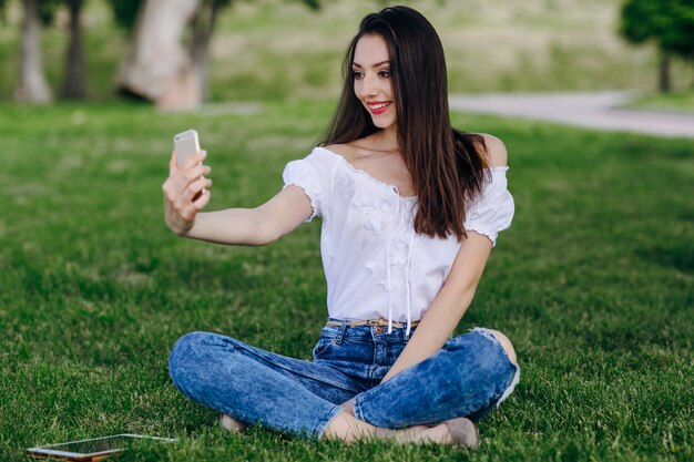 微笑しながら、自動写真を作る公園に座って若い女の子