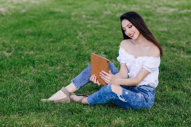 Young girl sitting in a park smiling while looking at an orange tablet