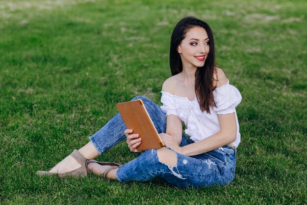 若い女の子の手でタブレットと公園で座って、側に見て