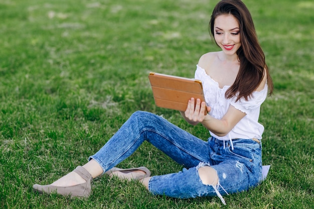 手の中にタブレットと公園に座って若い女の子