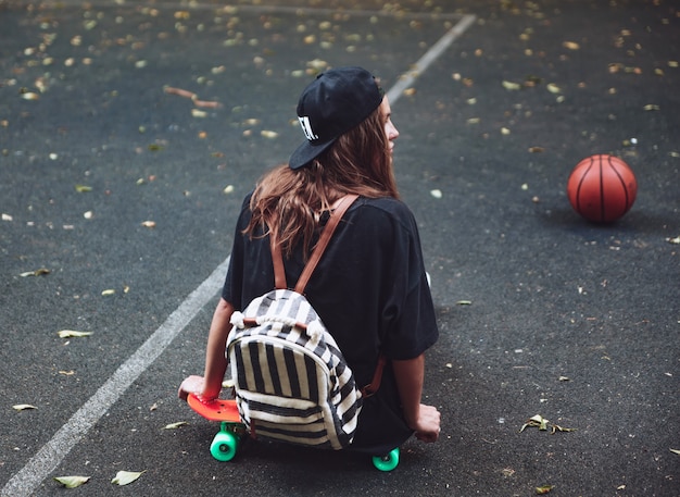 Foto gratuita ragazza che si siede sulla shortboard arancione di plastica del penny sull'asfalto in protezione