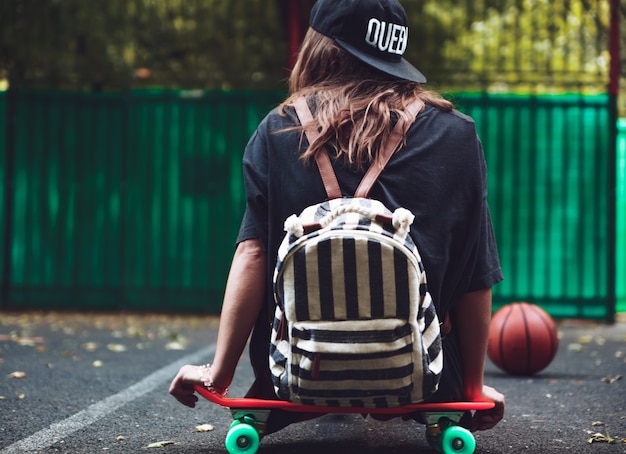 Foto gratuita ragazza che si siede sulla shortboard arancione di plastica del penny sull'asfalto in protezione