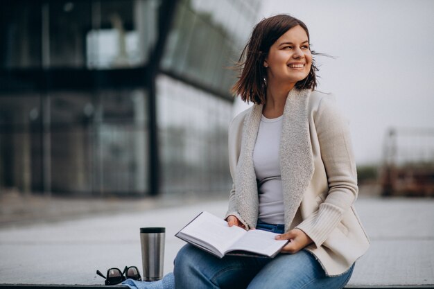 Young girl sitting reading book and drinking coffee outside the street