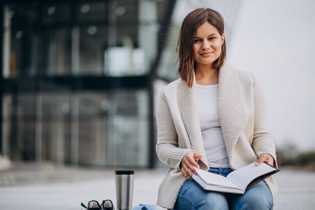 Young girl sitting reading book and drinking coffee outside the street