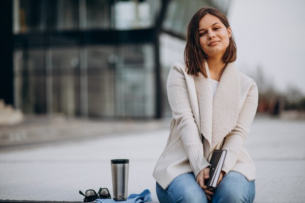 Young girl sitting reading book and drinking coffee outside the street