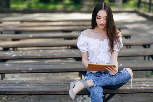 Young girl sitting on a wooden bench with a tablet