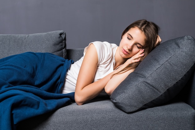 Young girl sleeping on a sofa covered with blue coverlet on gray background