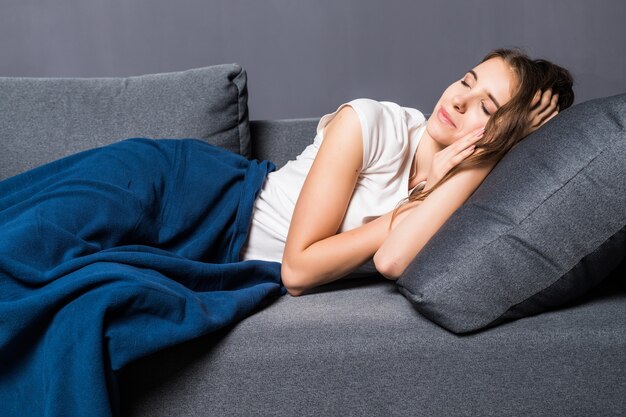 Young girl sleeping on a sofa covered with blue coverlet on gray background