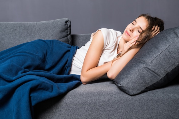 Молодая девушка спит на диване, покрытом синим покрывалом на сером фоне