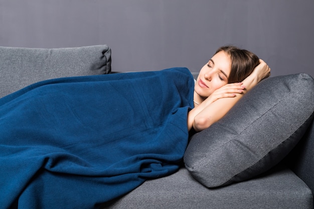 Young girl sleeping on a sofa covered with blue coverlet on gray background