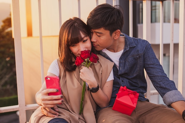 Young girl smelling some roses while her boyfriend takes a picture