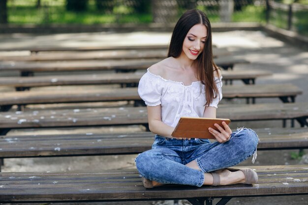 Young girl smiling and sitting on a wooden bench with a tablet