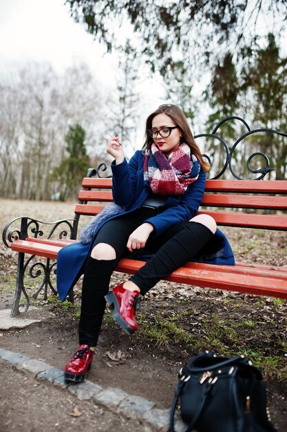 Young girl smoking cigarette outdoors sitting on bench Concept of nicotine addiction by teenagers