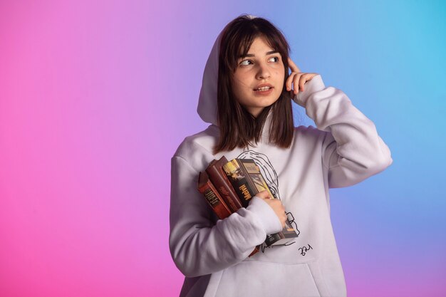 Young girl in sport outfits and short hairstyle holding books and thinking. 