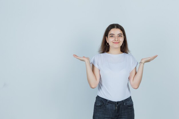 Tシャツ、ジーンズで横に手のひらを広げて、快適に見える、正面図の若い女の子。