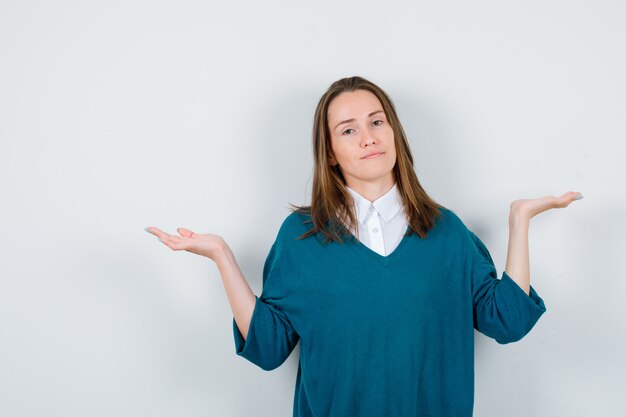 Young girl spreading palms in v-neck sweater, shirt and looking pensive , front view.