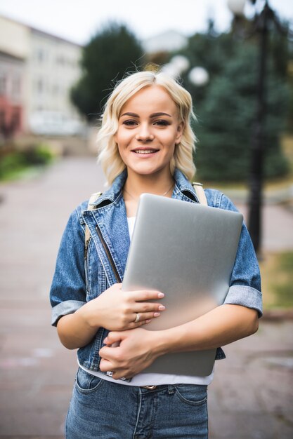 Young girl stand on the street with laptop in the city autumn morning