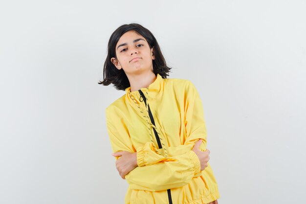 어린 소녀 서있는 팔은 노란색 폭격기 재킷과 심각한 찾고 넘어.