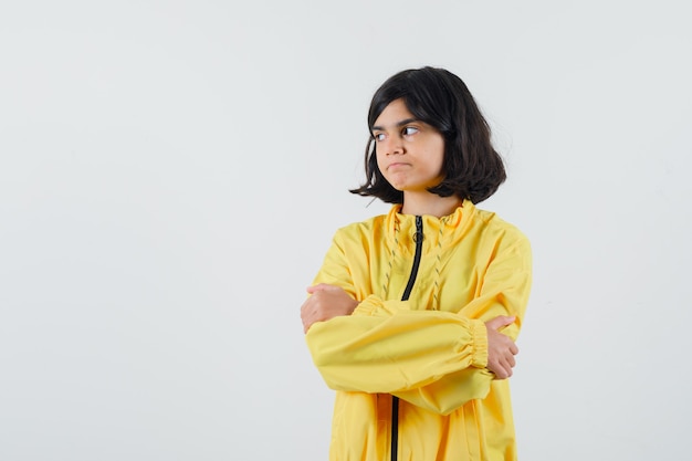 Молодая девушка стоя скрестила руки в желтой куртке бомбардировщика и выглядела серьезно.