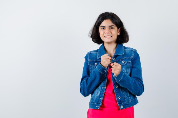 Young girl standing in boxer pose in red t-shirt and jean jacket and looking cheerful. front view.