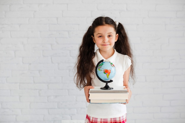 Free photo young girl standing holding books globe