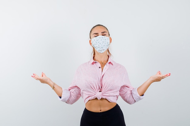 Young girl standing in meditating pose in pink blouse, black pants, mask and looking relaxed , front view.