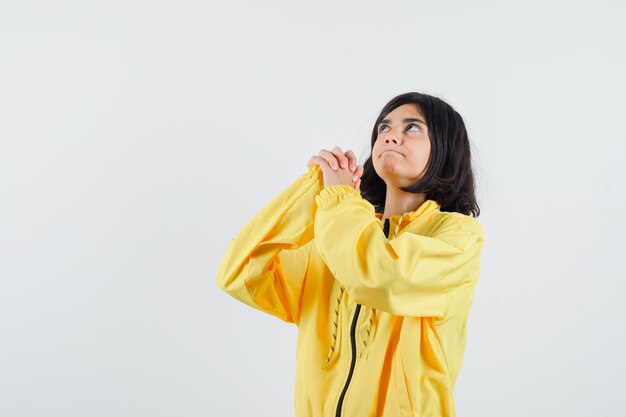 Young girl standing in prayer pose in yellow bomber jacket and looking focused