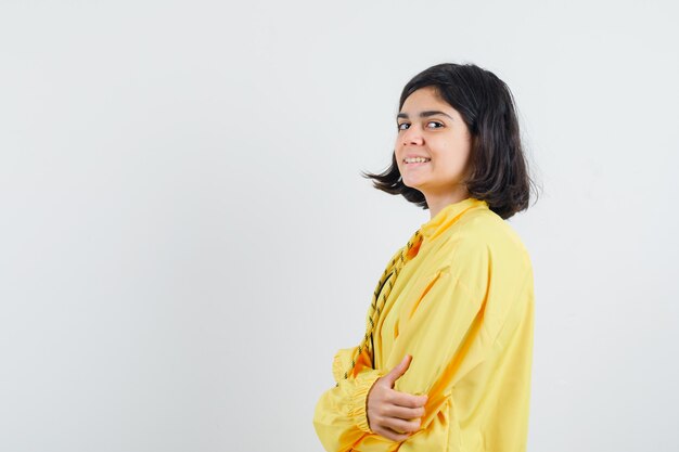 Young girl standing straight and looking over shoulder in yellow bomber jacket and looking happy