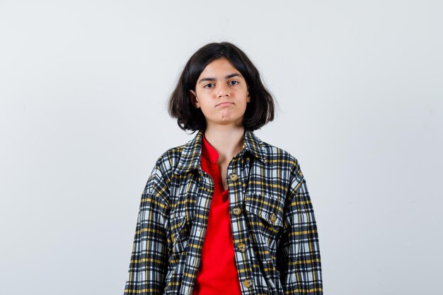 Young girl standing straight and posing at camera in checked shirt and red t-shirt and looking serious. front view.