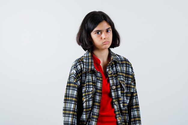 Young girl standing straight and posing at camera in checked shirt and red t-shirt and looking serious. front view.