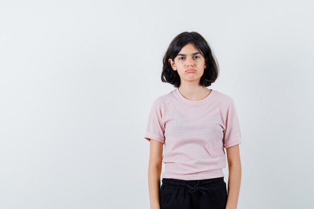 Young girl standing straight and posing at camera in pink t-shirt and black pants and looking cute