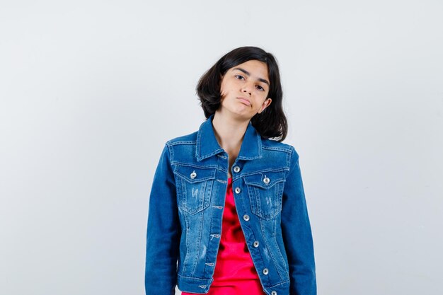 Young girl standing straight and posing at camera in red t-shirt and jean jacket and looking cute. 